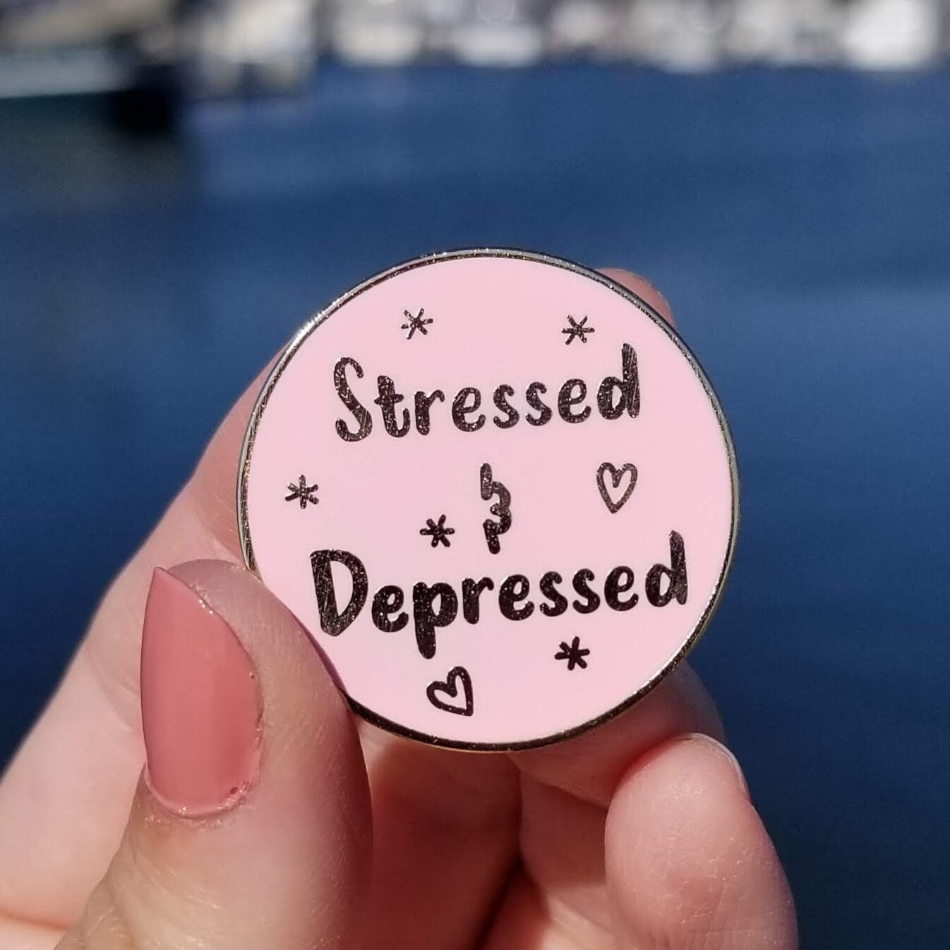 Pink round pin with 'Stressed & Depressed' text held by a hand against a blue background