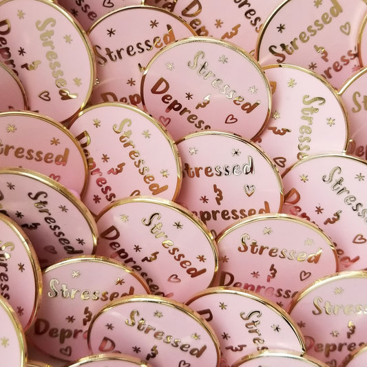 Pink and gold pin buttons with 'Stressed' and 'Depressed' text on a pink background
