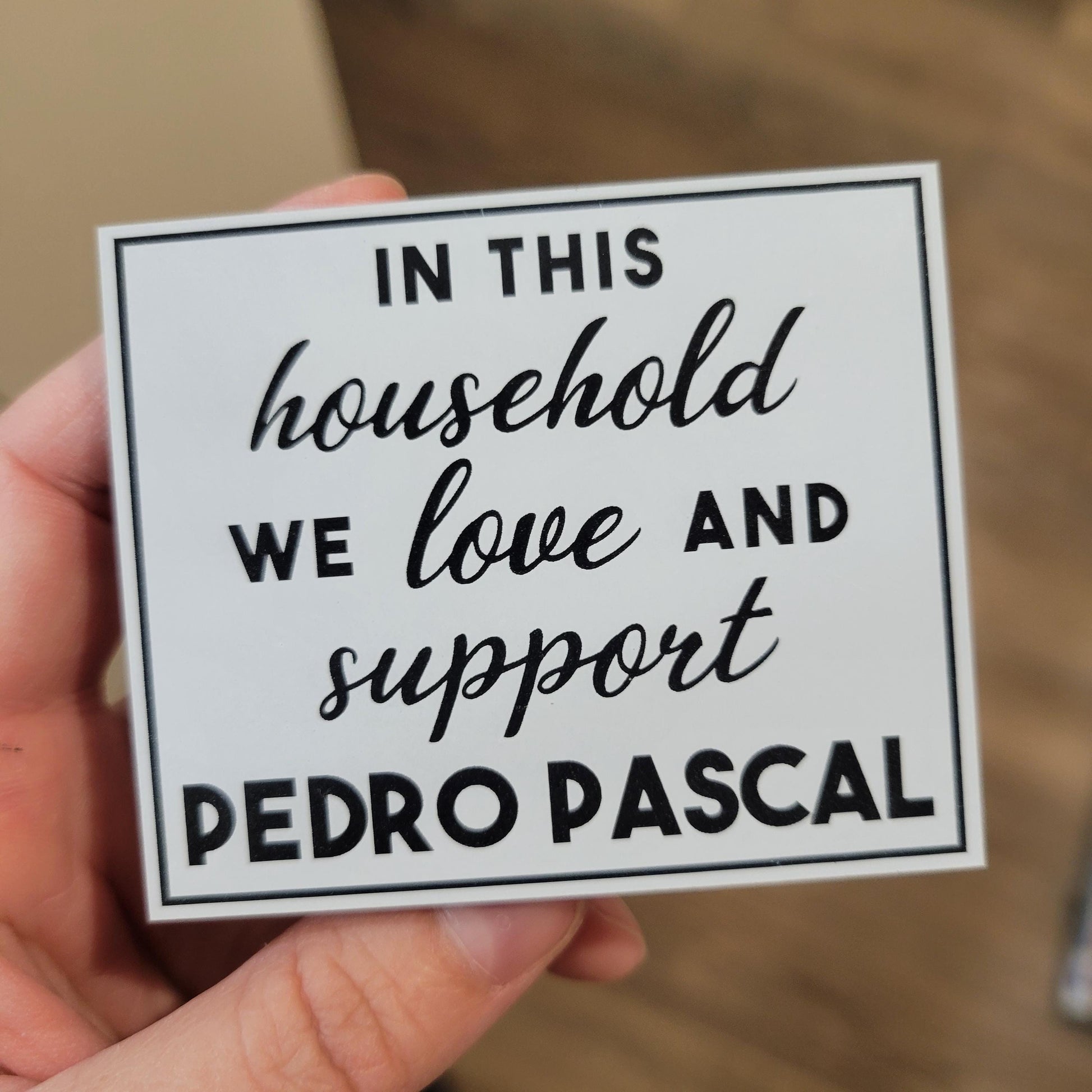 Hand holding a sign with text 'In this household we love and support Pedro Pascal'