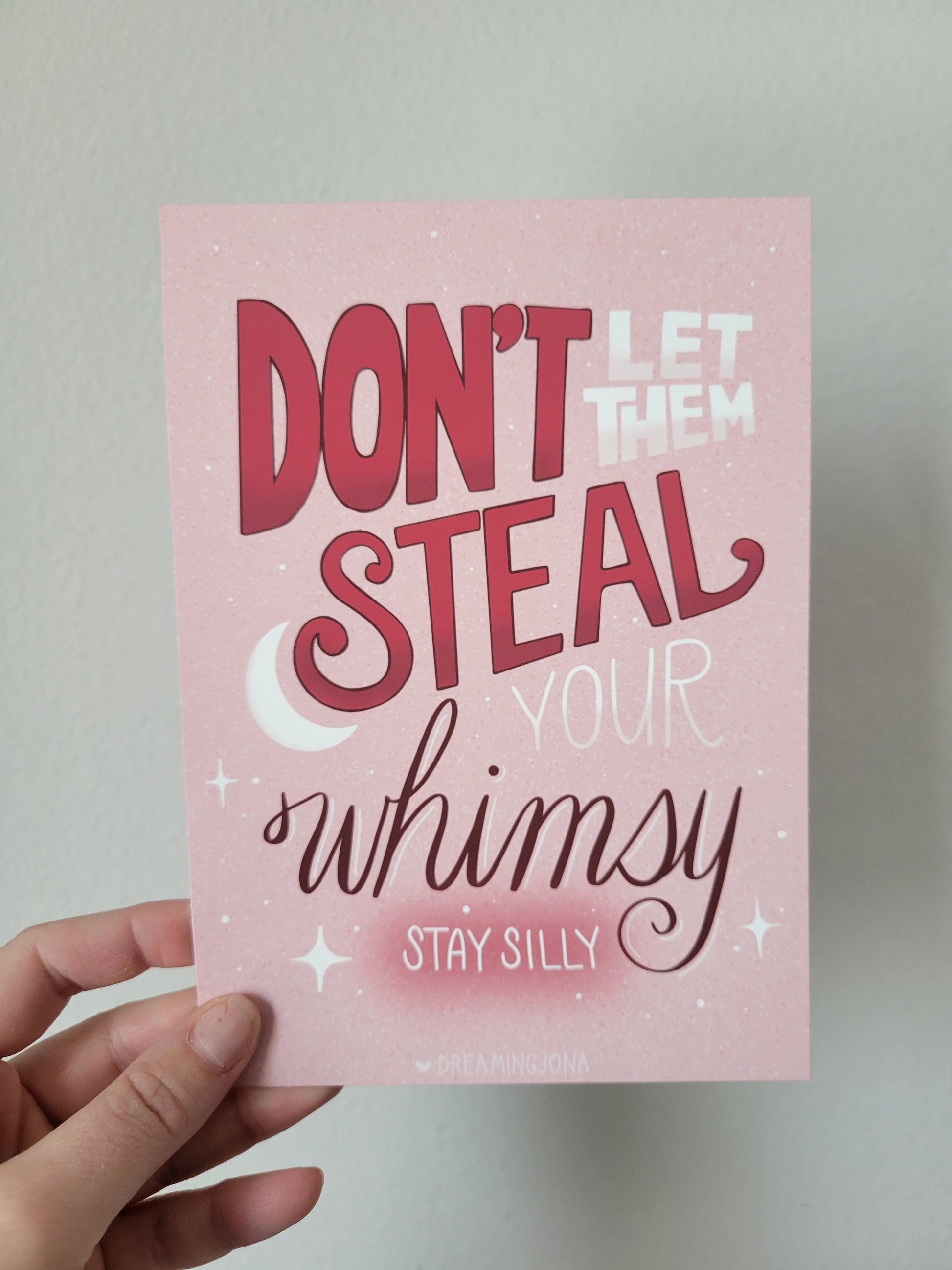Hand holding a pink card with motivational text on a light gray background